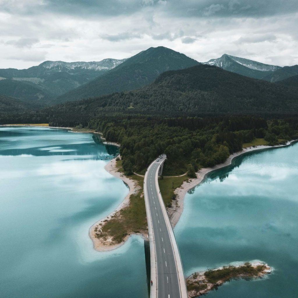 gray asphalt road with body of water under blue sky during daytime